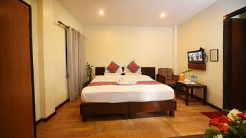 Una habitación de hotel con una cama grande, suelo de madera, una pequeña mesa con una planta y un televisor en la pared.