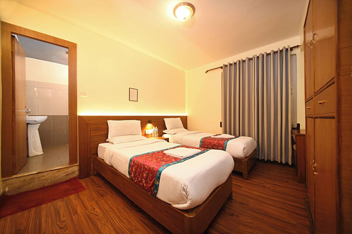 A hotel room with two beds, a wooden wardrobe, a mirror, and a bathroom visible through an open door.