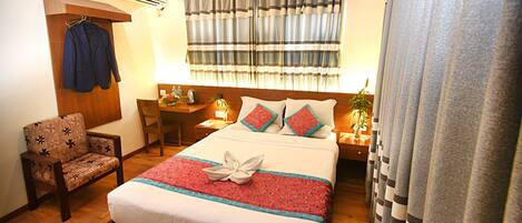 A neatly arranged hotel room with a bed, a chair, a desk, and a nightstand.
