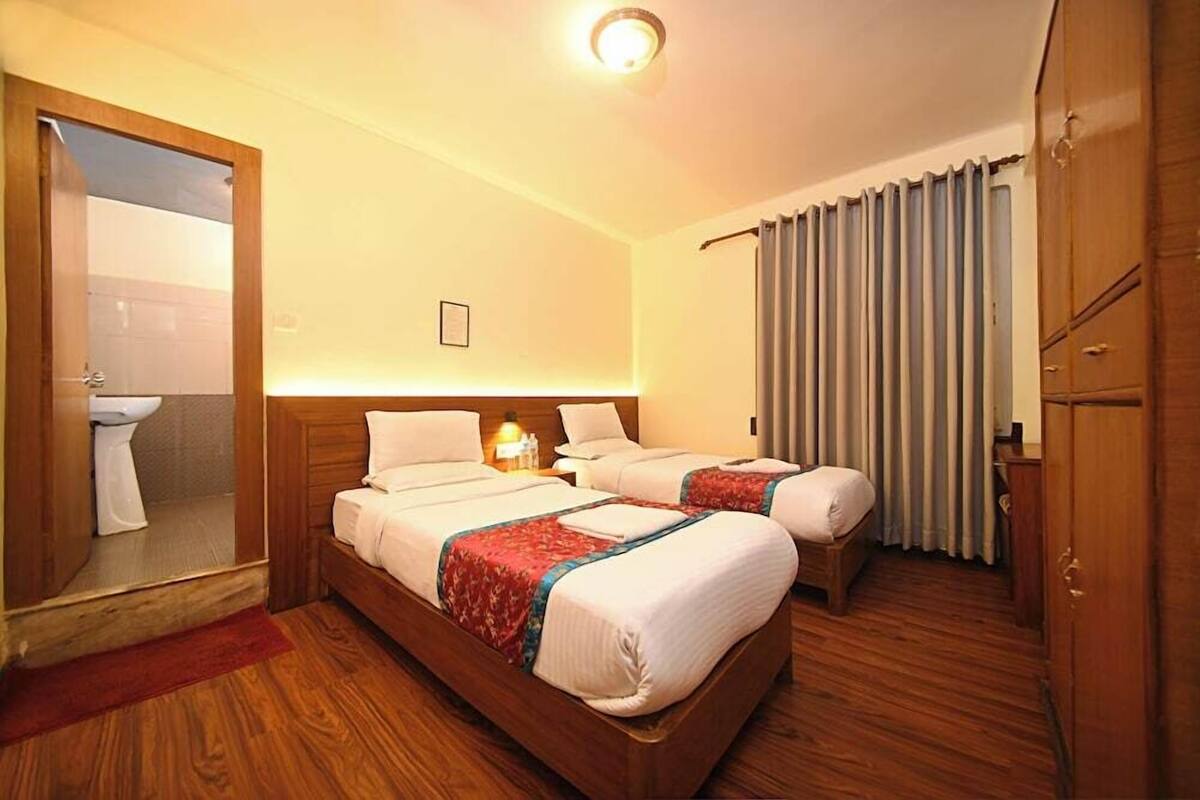 A hotel room with two beds, a wooden wardrobe, a bathroom with a toilet, and a mirror.