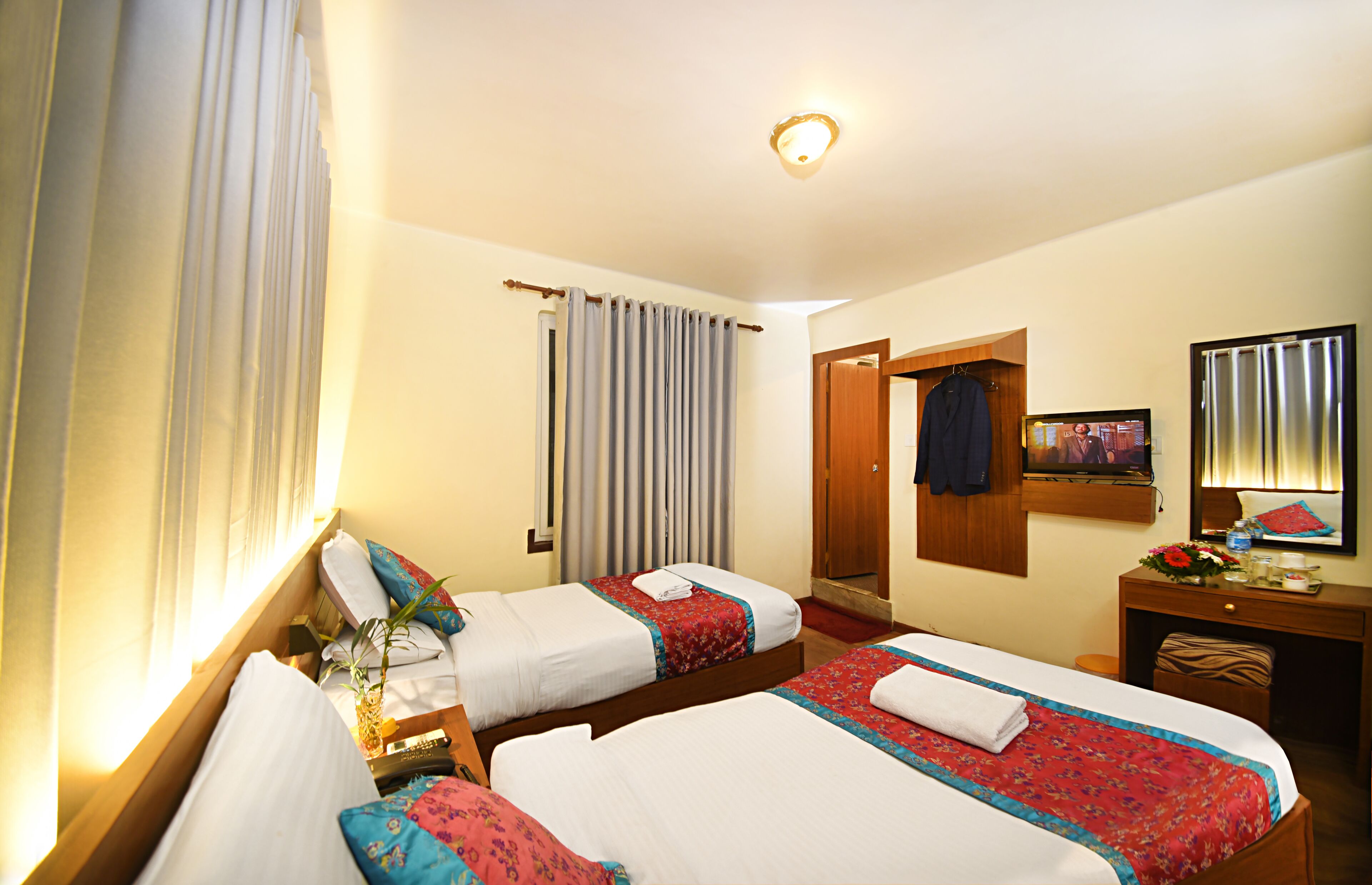 A hotel room with two beds, a desk, a mirror, and a television.