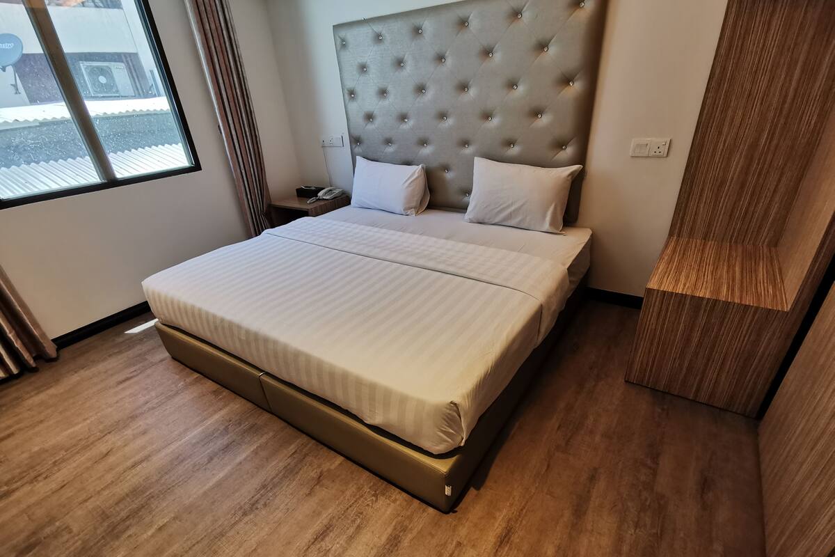 A modern hotel room with a large bed, a tufted headboard, a bedside table with a phone, and a window with curtains.