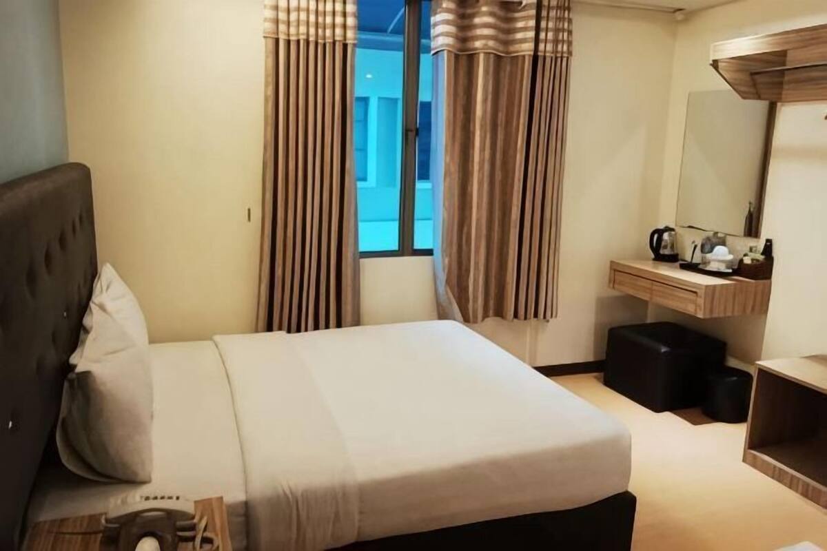 A hotel room with a bed, a desk, a mirror, a window with curtains, and a view of the outside.