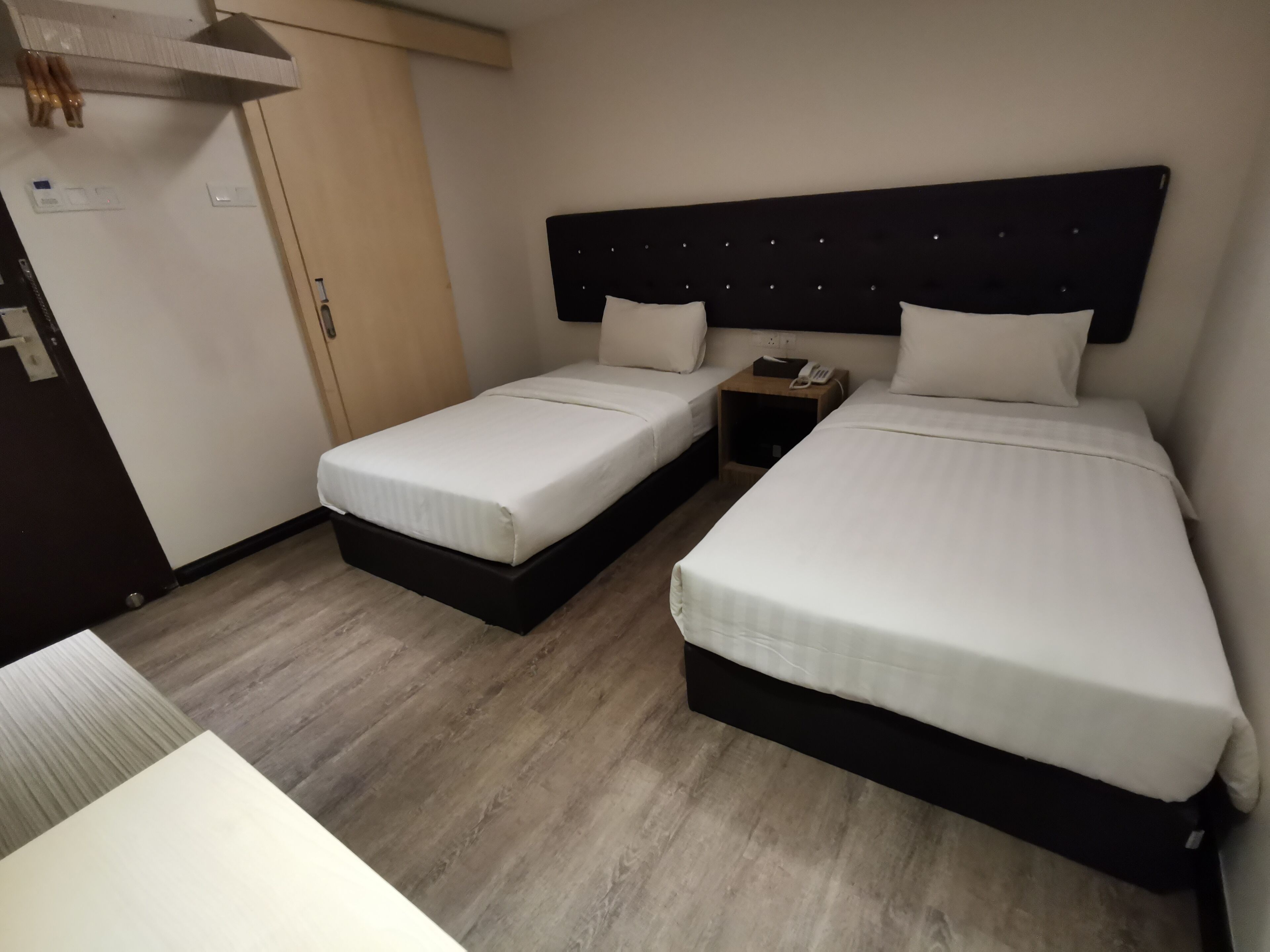 Habitación de hotel con dos camas individuales, piso de madera, una mesita de noche con teléfono y un armario.