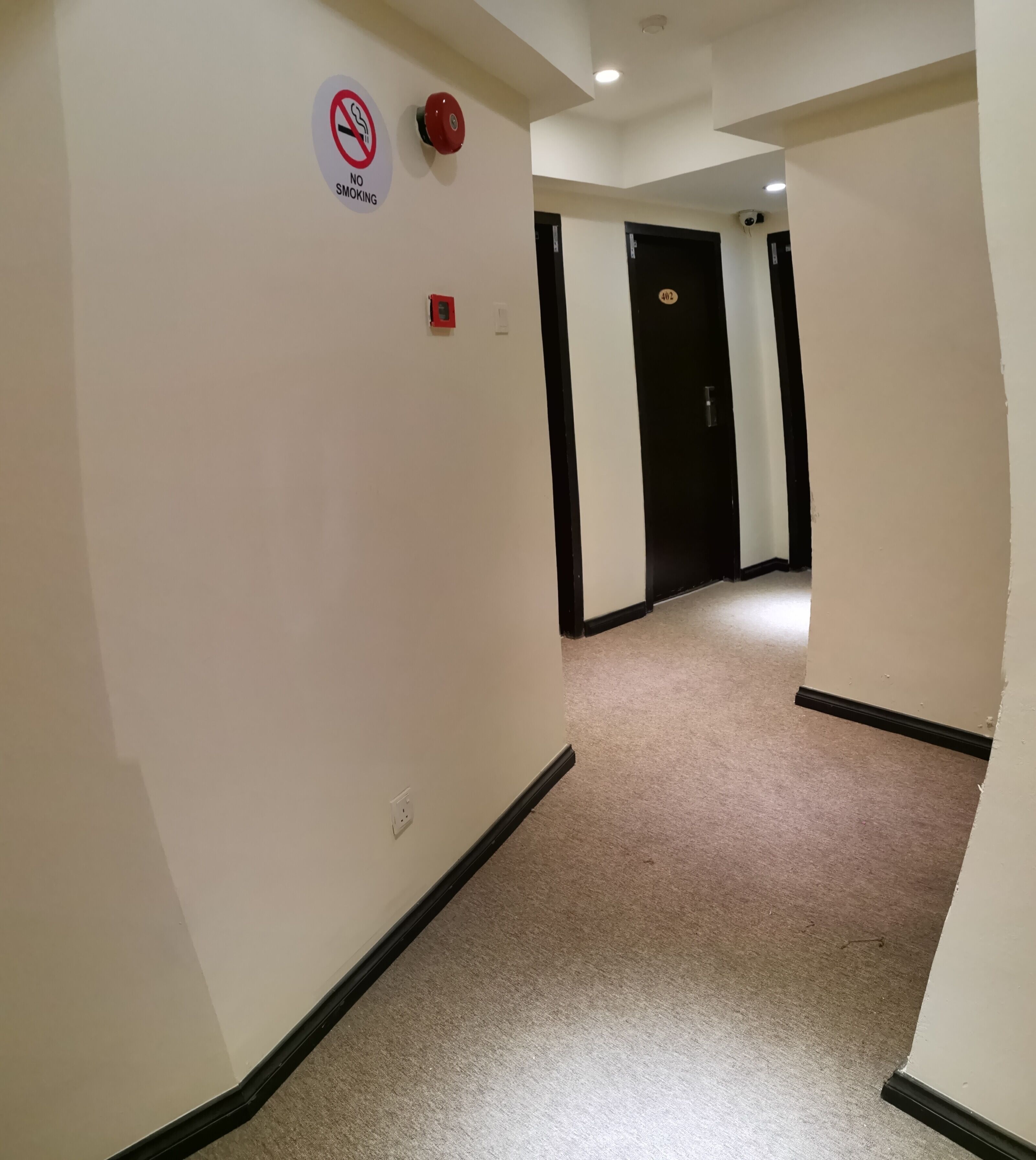 A hallway with a 'No Smoking' sign, a fire alarm, and a door with a number plate.