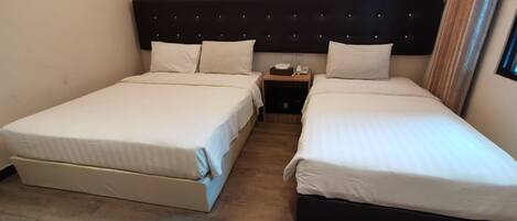 Quarto de hotel com duas camas de solteiro, cabeceira escura, mesa de cabeceira com telefone e lenços, e piso de madeira.