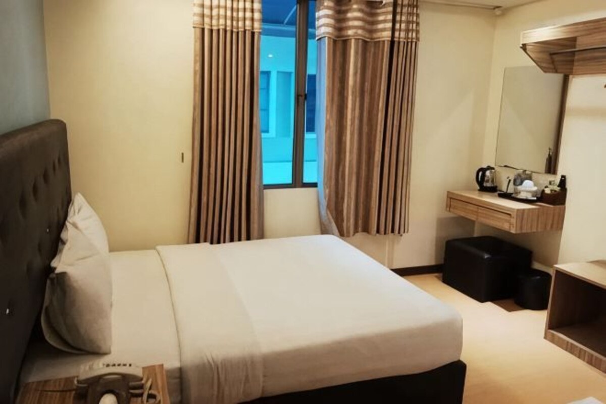 A hotel room with a bed, a desk, a mirror, a window with curtains, and a view of the outside.