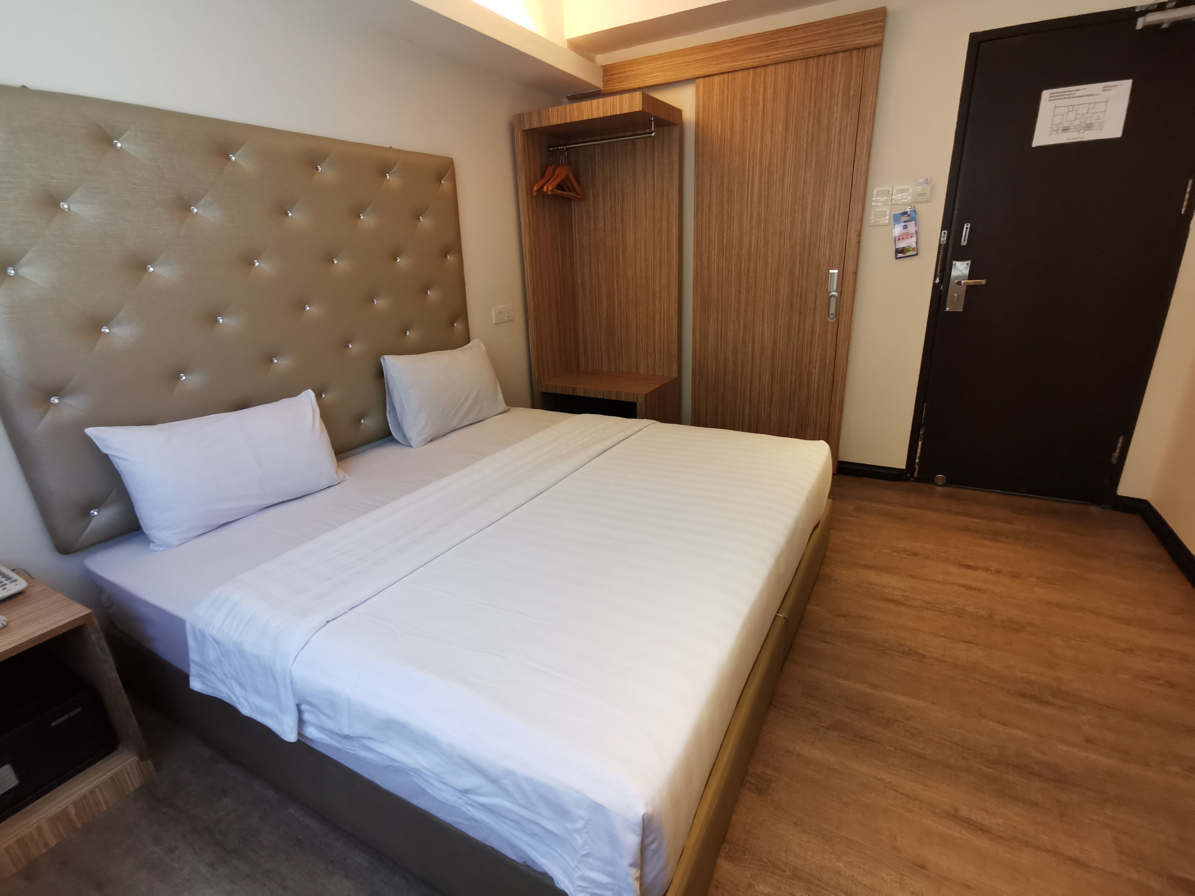 A hotel room with a large bed, a wooden headboard, a wardrobe, and a door with a notice.