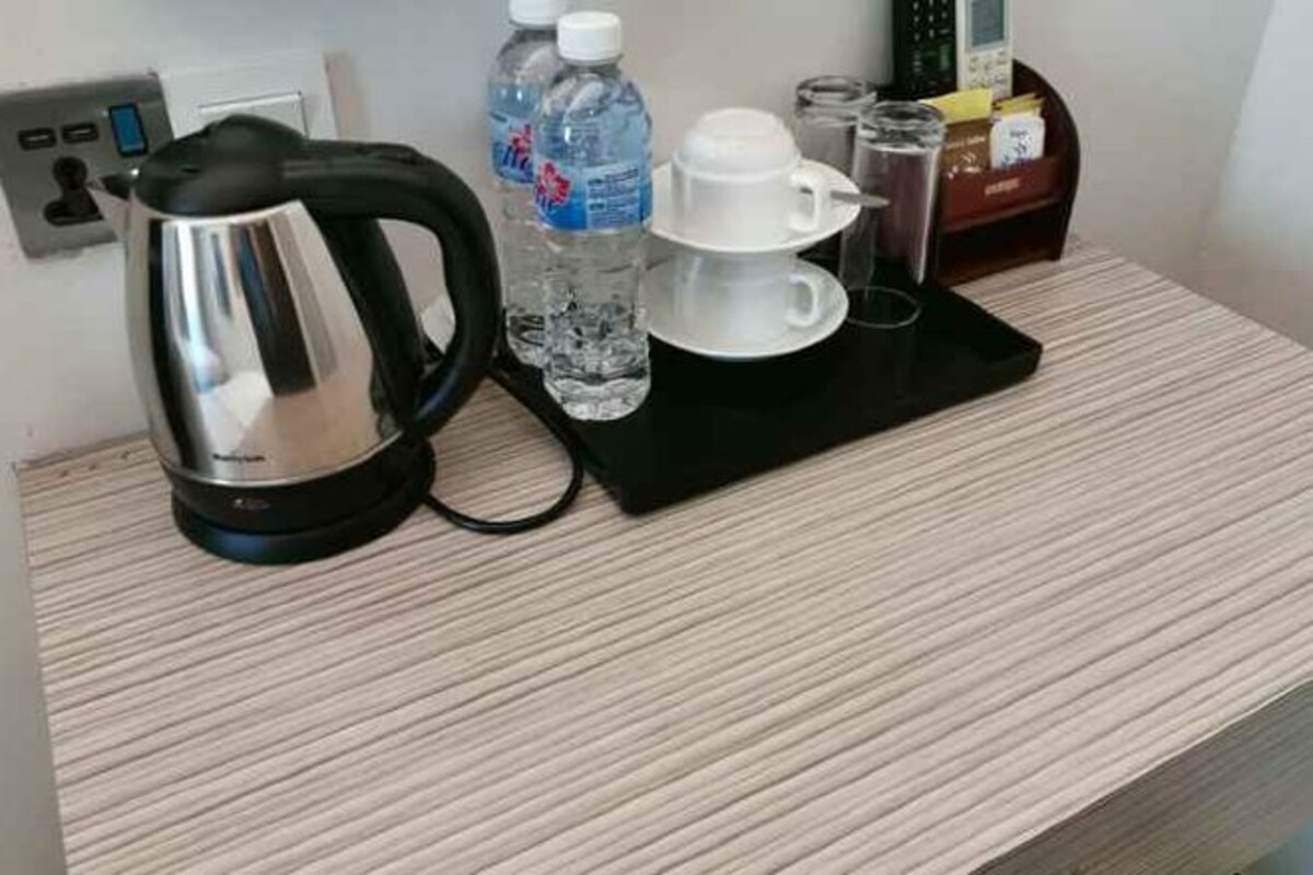 A kitchenette with a kettle, water bottle, cups, and a glass.