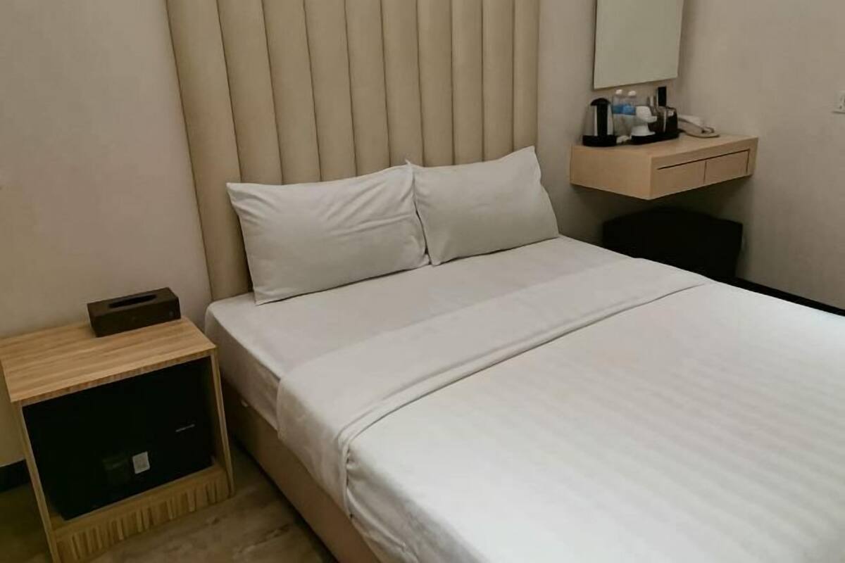 A hotel room with a bed, a bedside table, a nightstand, a mirror, and a small wooden cabinet.