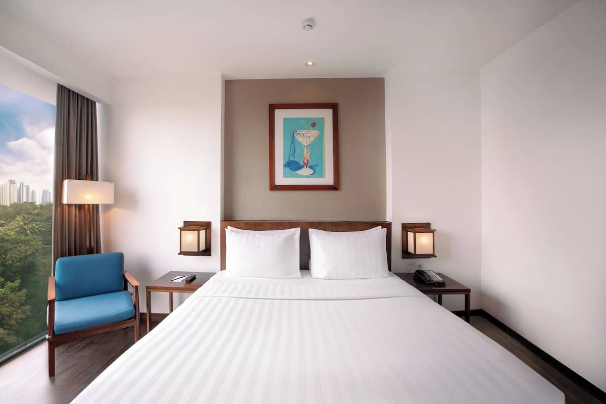 A hotel room with a large bed, a blue armchair, a nightstand with a lamp, and a framed picture on the wall.