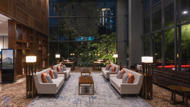 A modern lobby with two sofas facing a central coffee table, surrounded by floor lamps and a large window offering a view of city buildings. - Veranda Hotel Pakubuwono (Jakarta)