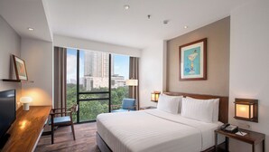 A hotel room with a large bed, a desk with a chair, a TV, and a city view through the window. - Veranda Hotel Pakubuwono (Jakarta)
