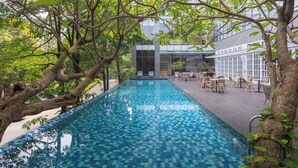 A rectangular outdoor pool with a checkered tile pattern, surrounded by trees and a building with a glass facade. - Veranda Hotel Pakubuwono (Jakarta)
