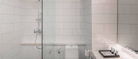 Ein modernes Badezimmer mit weißen Fliesen, einer Duschkabine, einer Toilette und einem Waschbecken mit Pflegeprodukten.