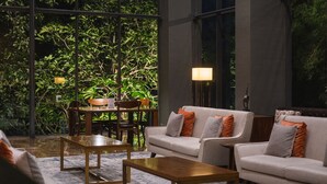 A modern living room with a sofa set, a coffee table, and a dining table with chairs. There is a large window with a view of lush greenery outside. - Veranda Hotel Pakubuwono (Jakarta)