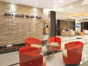 A lobby with a reception desk, red chairs, and a stone wall with the hotel name. - Ayara Grand Palace Hotel (Phitsanulok)