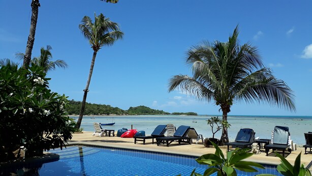 A poolside area with lounge chairs, a clear blue sky, and a view of the ocean. - Papillon Resort (Koh Samui)