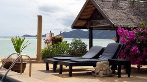 A beachside lounge with two sun loungers, a thatched-roof structure, and a view of the sea and mountains. - Papillon Resort (Koh Samui)