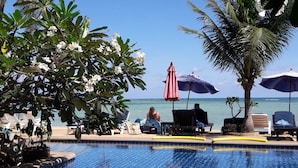 A poolside area with lounge chairs, umbrellas, and a view of the ocean. - Papillon Resort (Koh Samui)