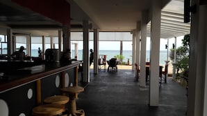 A spacious indoor area with a view of the sea, featuring a bar area with stools and tables, and a seating area with chairs and a table. - Papillon Resort (Koh Samui)