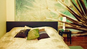 Una cama con cabecera oscura, varios almohadones y una pared decorativa con motivos de plumas de pavo real.