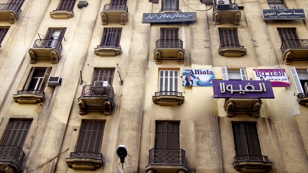 Un edificio con varios balcones, unidades de aire acondicionado y diversos letreros en árabe.
