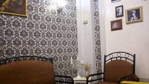 Una habitación con papel tapiz estampado, un sofá, una silla, una mesita y una pared decorada con cuadros.