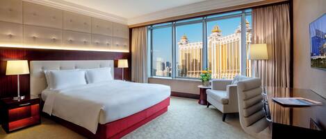 A hotel room with a large bed, a desk, a chair, and a window with a view of a building.