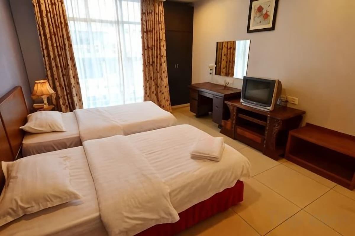 A hotel room with two beds, a desk, a television, and a mirror.