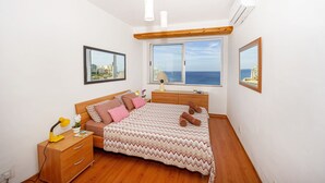 Un dormitorio con cama, mesita de noche, lámpara y ventana con vista al mar.