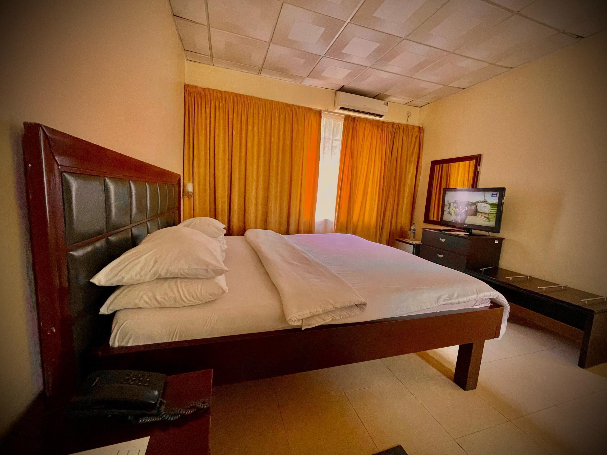 A hotel room with a large bed, a television, a desk, and a wardrobe.