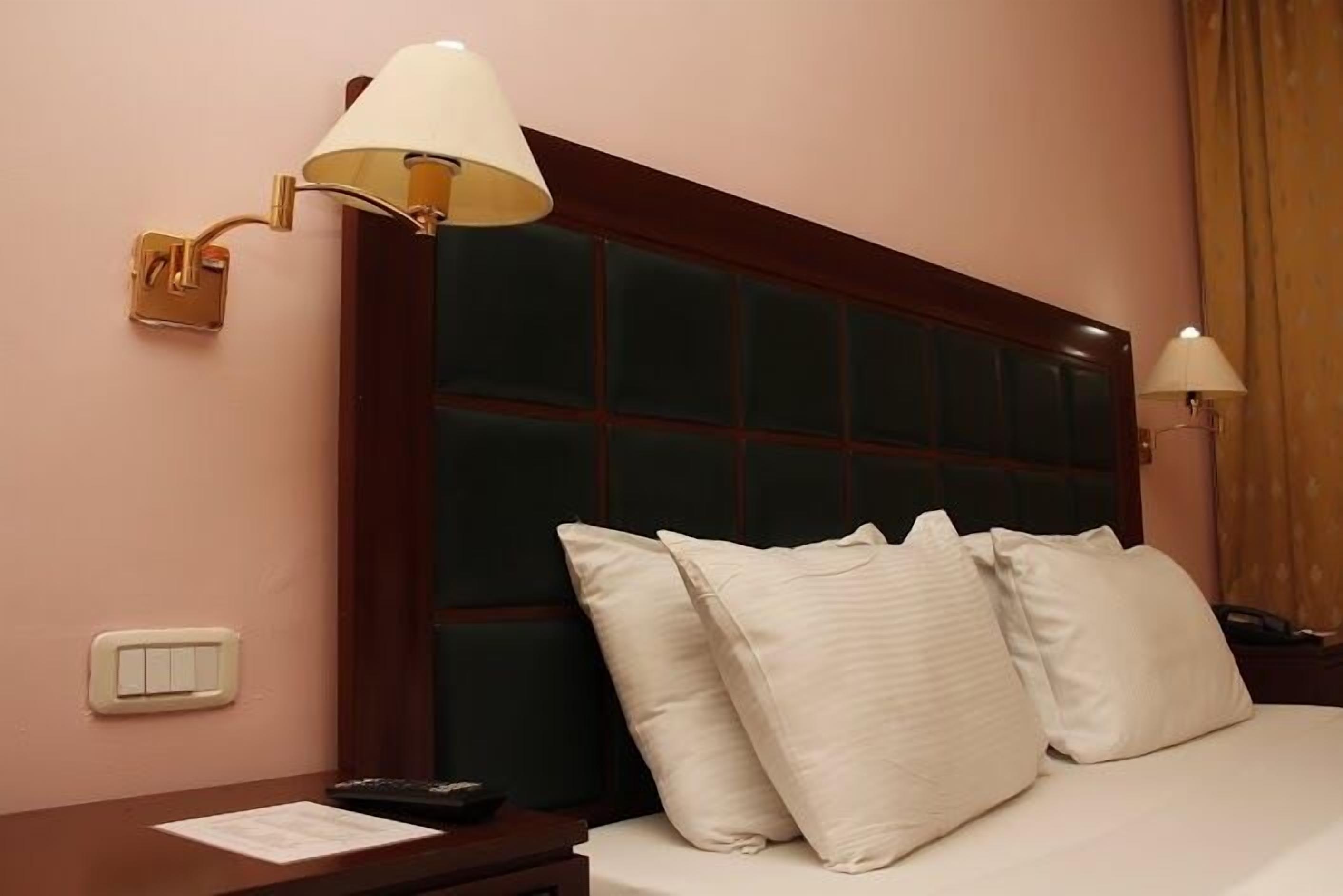 Habitación de hotel con una cama grande, dos lámparas de noche, una mesita de noche y un interruptor de pared.
