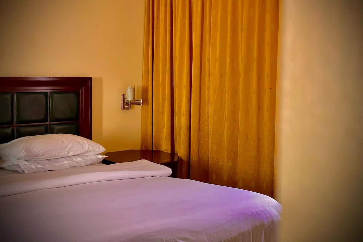 A hotel room with a bed, a nightstand, and a wall-mounted lamp.