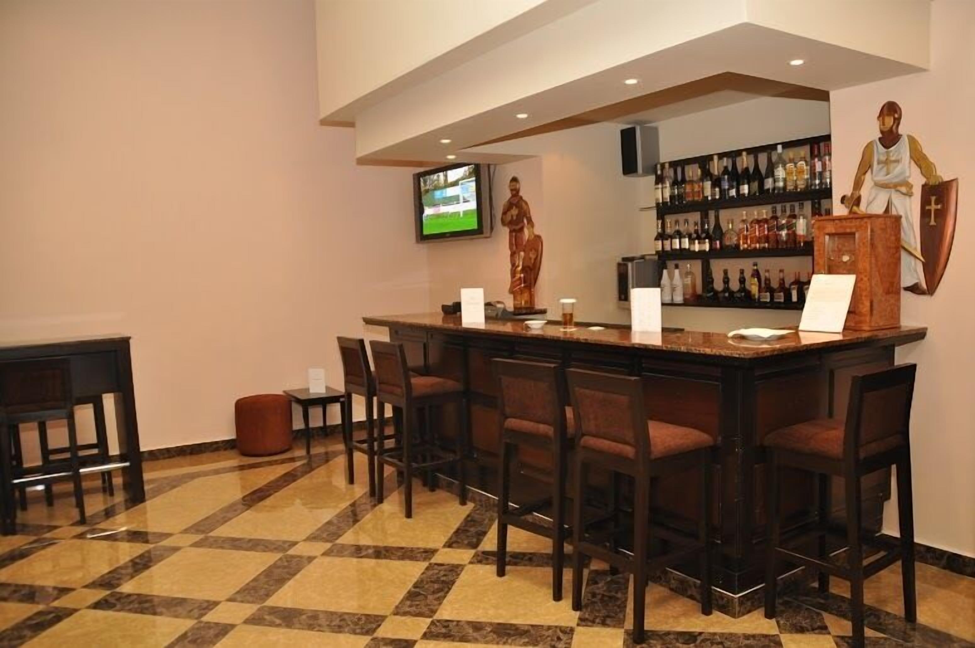 A bar area with a checkered floor, a television mounted on the wall, and a statue of a person.