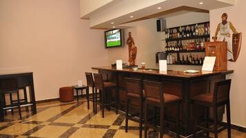 A bar area with a checkered floor, a television mounted on the wall, and a statue of a person.