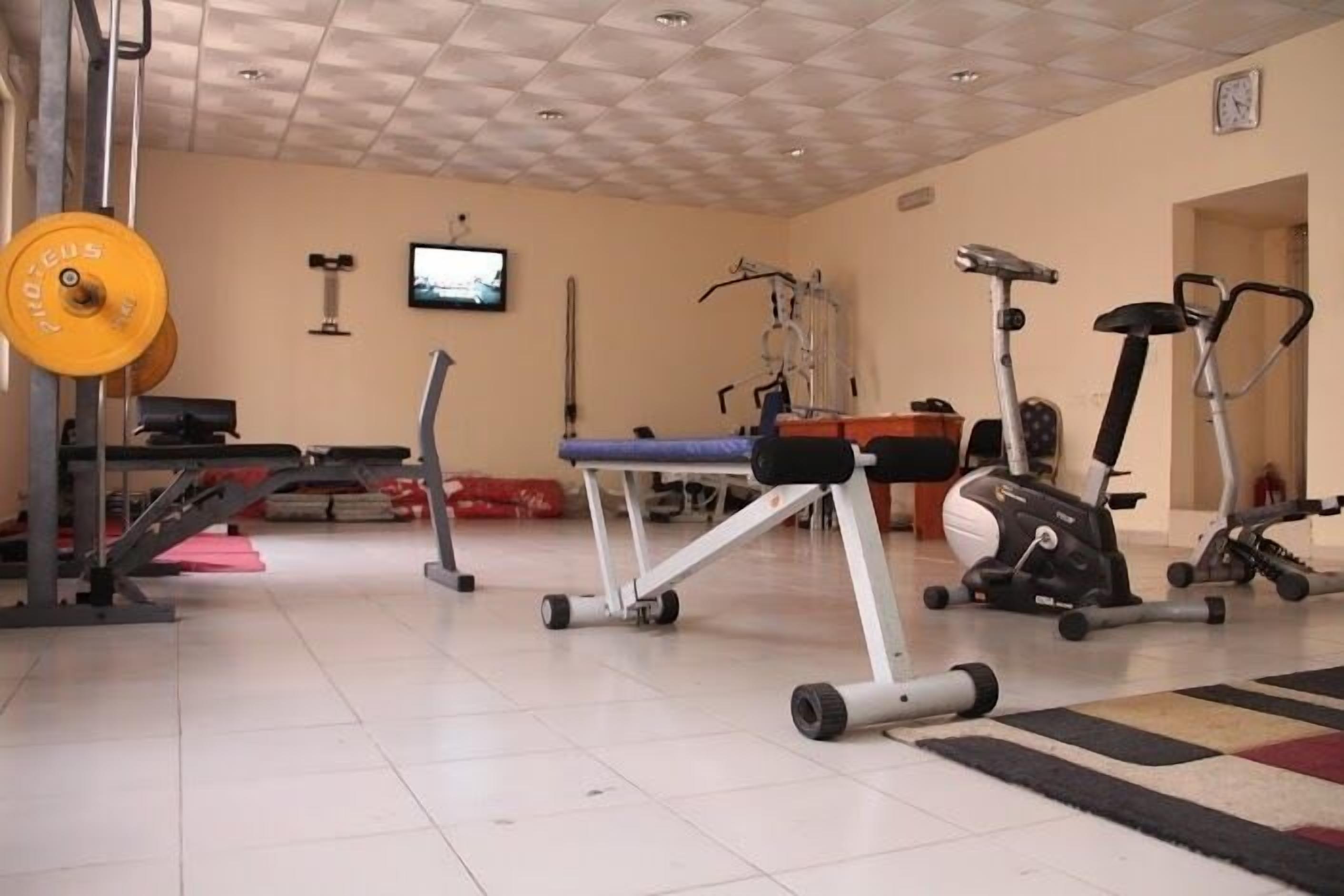 Un gimnasio con equipo de ejercicio, un televisor y un reloj en la pared.