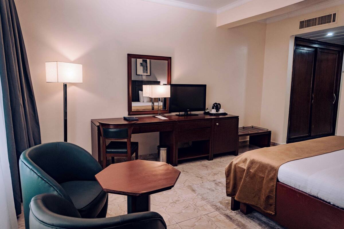 A hotel room with a bed, desk, chair, lamp, television, and wardrobe.