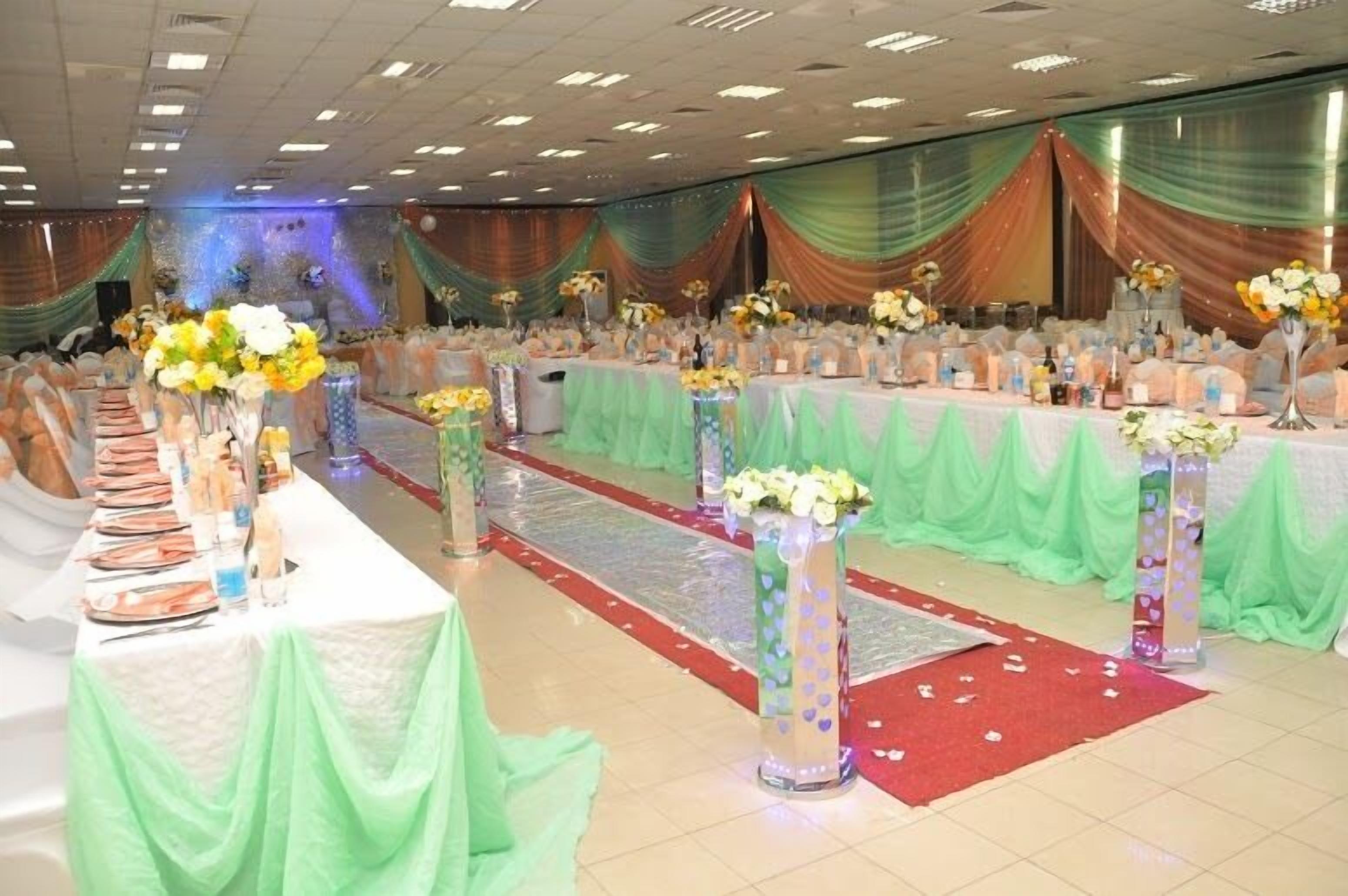 A banquet hall with tables set for a formal event, draped with green fabric and adorned with floral centerpieces.