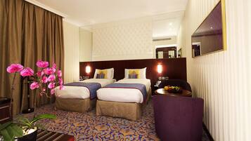A hotel room with two beds, a large mirror, a small table with fruit, and a potted plant.