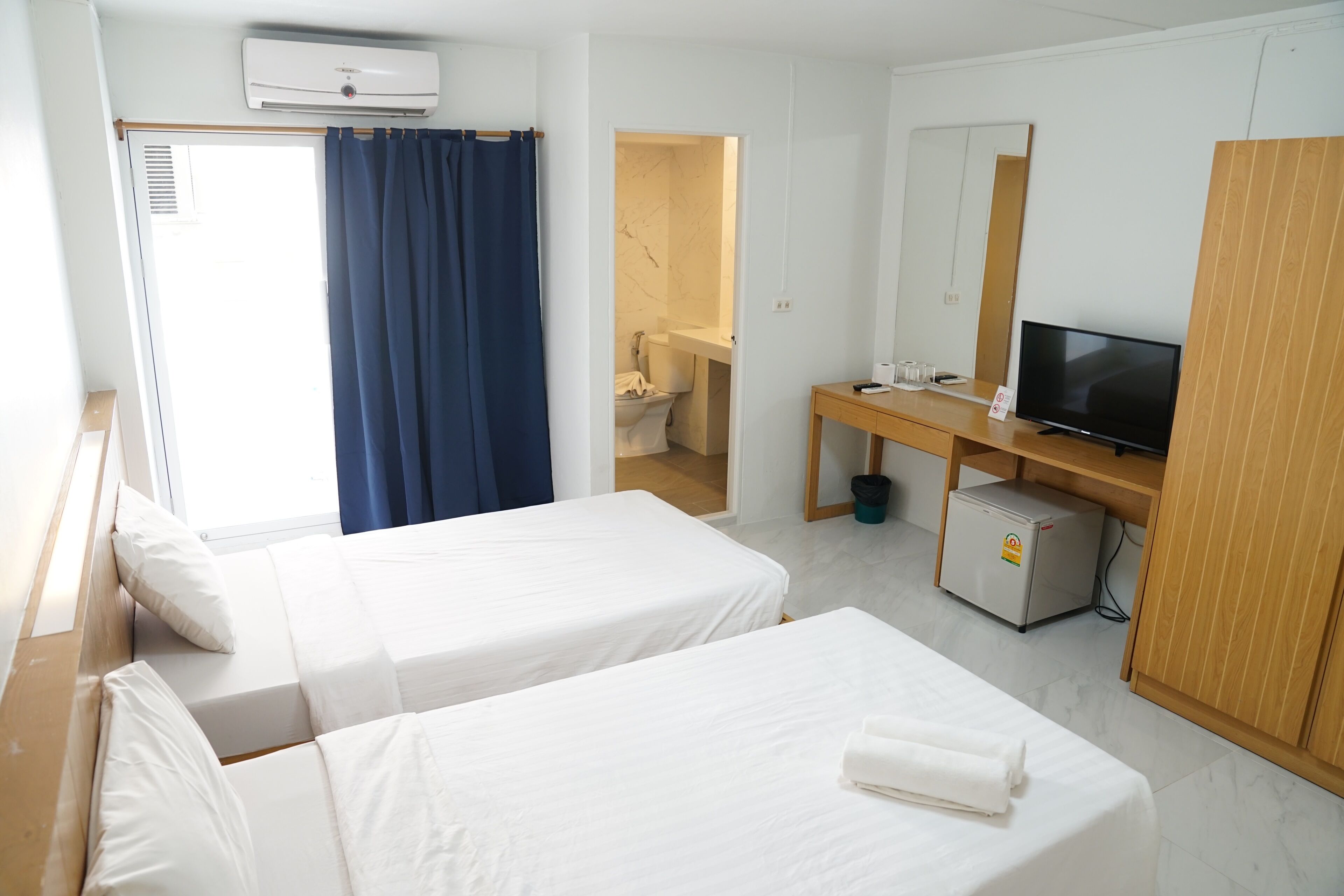 A hotel room with two beds, a TV, a desk, and a small fridge.