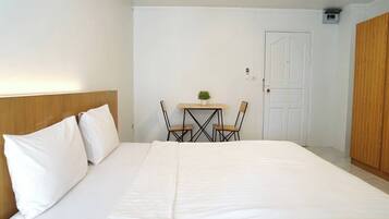 A bedroom with a large bed, a wooden headboard, a small table with two chairs, a potted plant, and a door.