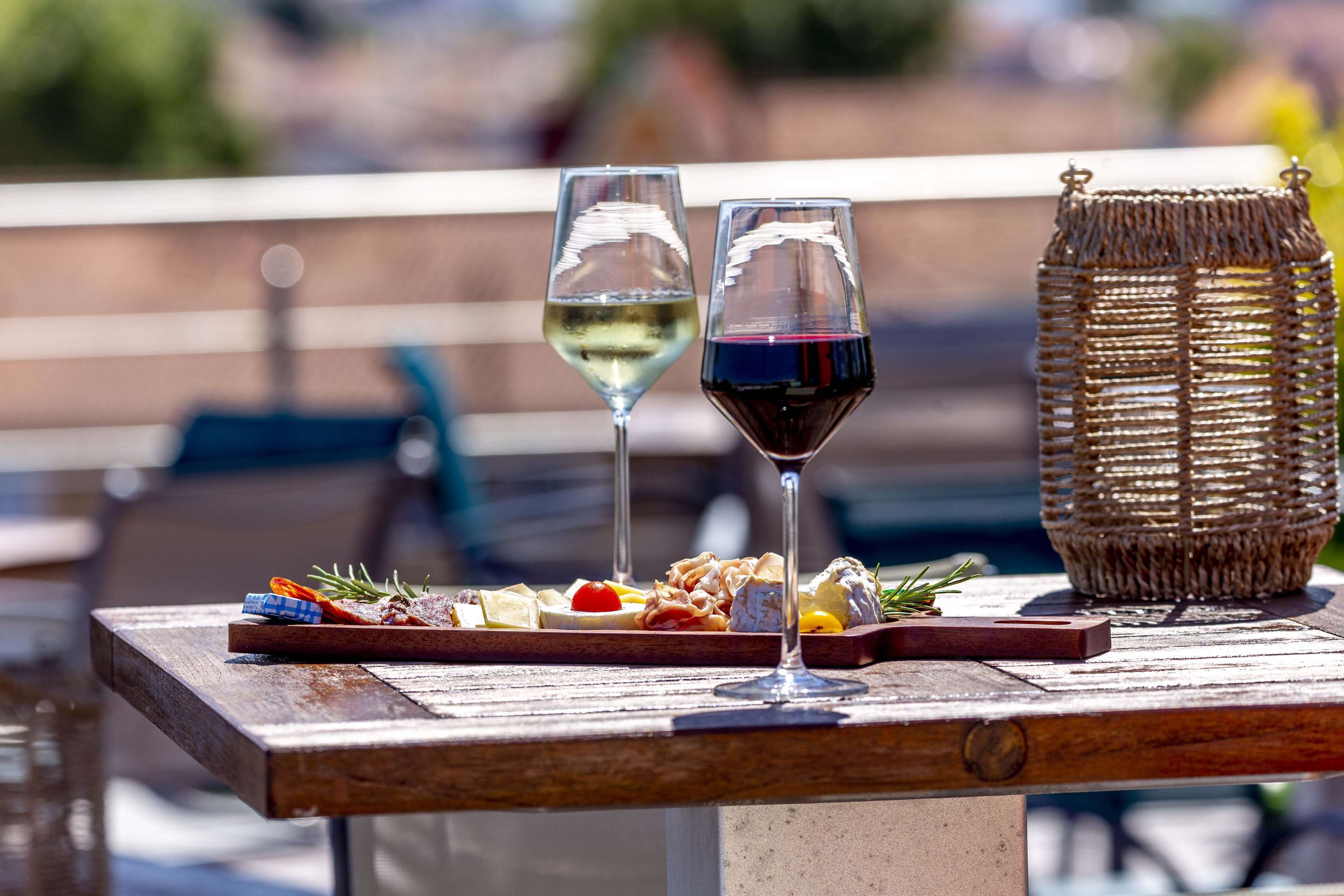 A wooden table with a charcuterie board and two wine glasses, one with white wine and the other with red wine, set outdoors.