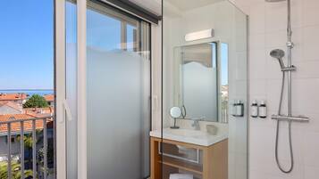 Une salle de bain moderne dotée d’une douche à parois de verre, d’un meuble-lavabo avec miroir et offrant une vue sur le paysage urbain.