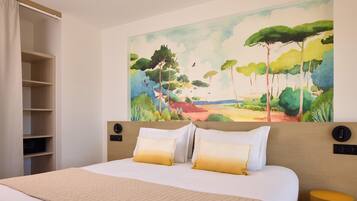Una habitación de hotel con una cama, un cuadro grande de paisaje en la pared, un armario y una mesita de noche.