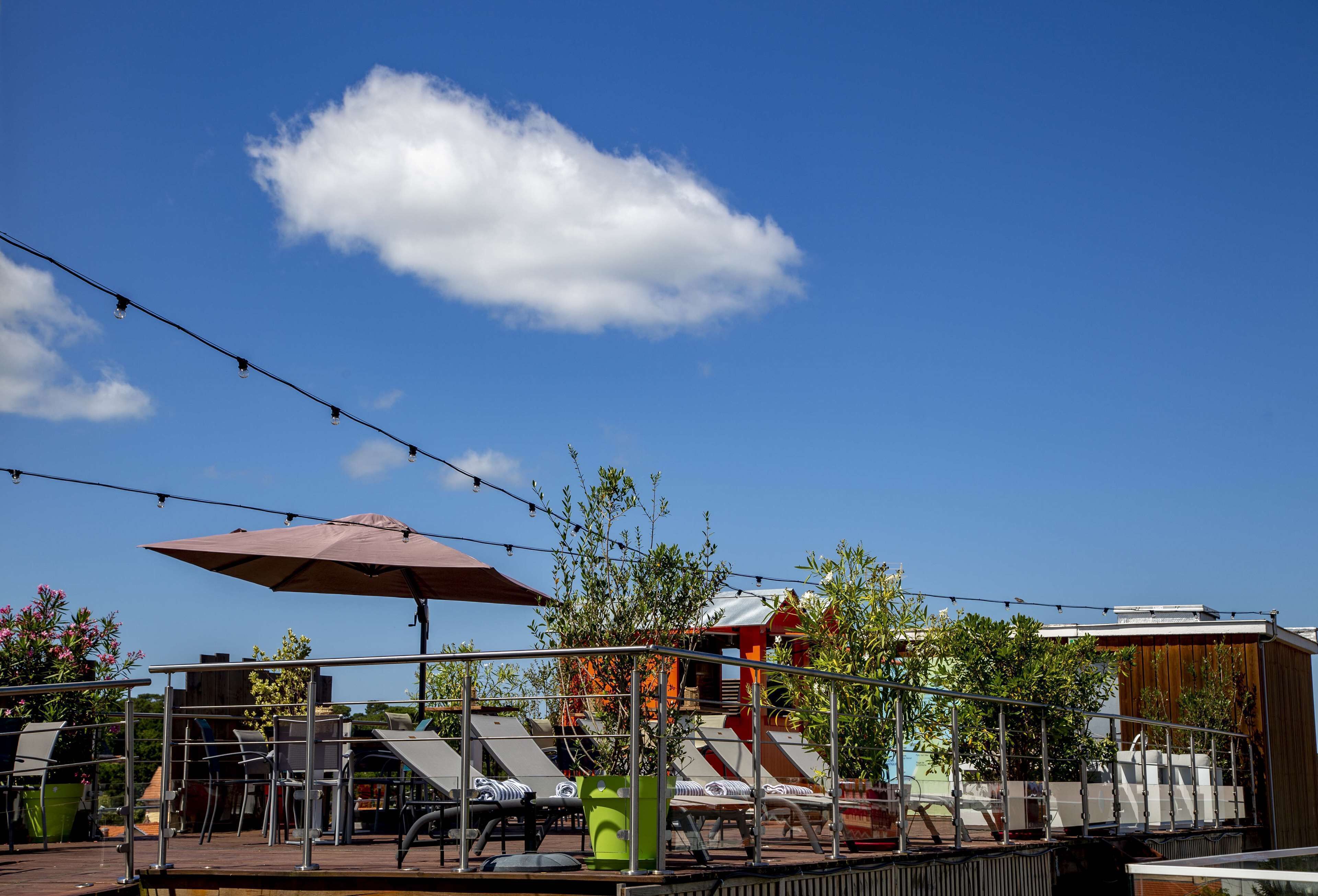 Un espace extérieur aménagé avec des parasols, des chaises et des guirlandes lumineuses, le tout sur fond de ciel dégagé.
