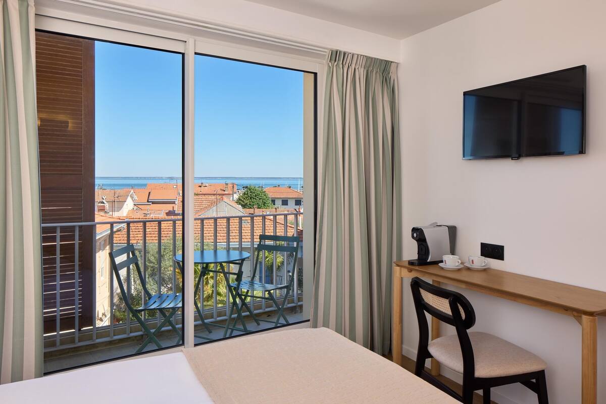A hotel room with a balcony, a desk with a chair, a television, and a bed.