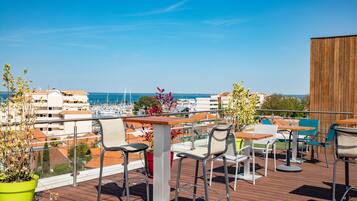 Una terraza con mobiliario exterior, una cubierta de madera y vistas al puerto deportivo y edificios.
