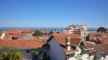 A coastal residential area with terracotta-tiled roofs, white and green buildings, and a clear blue sky.