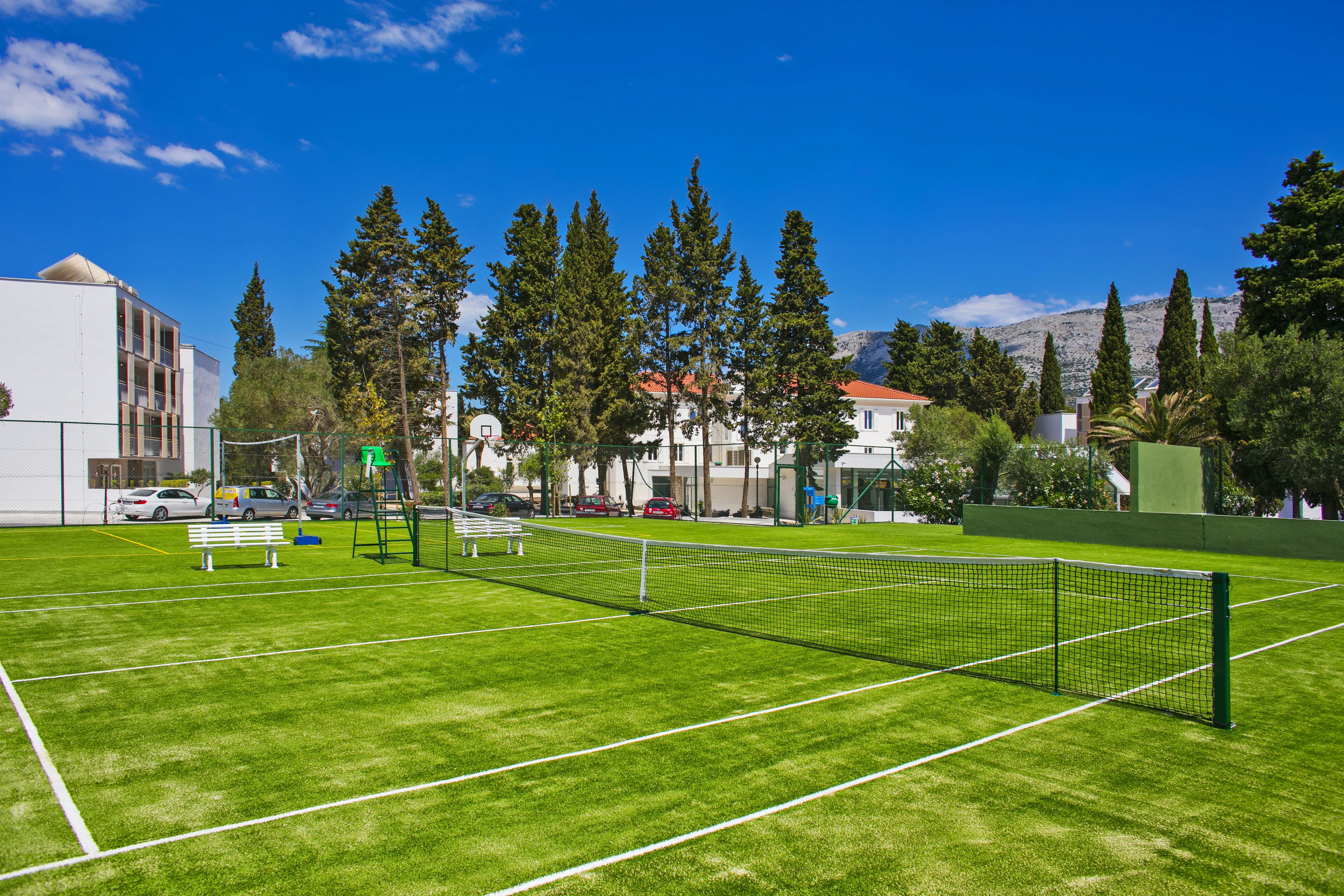 A tennis court with a net, surrounded by trees and buildings.